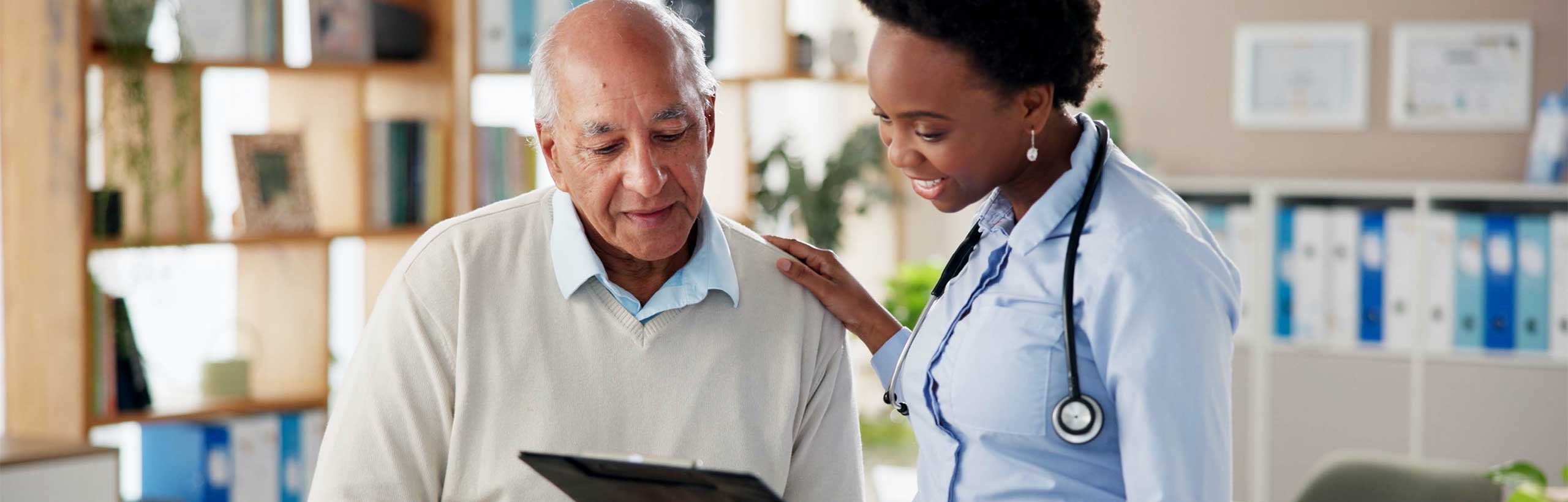 An African-American doctor reviews a form that a patient brought in. She stands in a comfortable office with homey furnishings but also bookshelves filled with binders of paperwork. A gray-haired patient looks at the form with the doctor. Their relaxed expressions show that the process is going well.